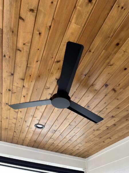 A black three-blade ceiling fan is mounted on a wooden plank ceiling with a recessed light nearby, adding stylish details perfect for your Oahu remodeling project.